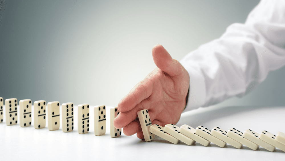 Close-up of a male hand preventing a line of dominoes from falling - signifying the concept of risk